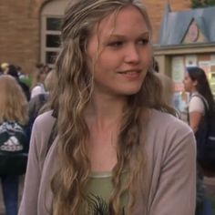 a young woman with long hair standing in front of a building and looking at the camera