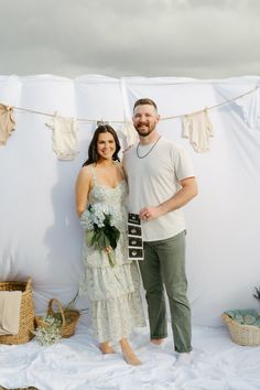 a man and woman standing next to each other in front of a white wall with clothes hanging on it