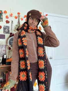 a woman wearing a brown hat and scarf with orange flowers on it, standing in front of a white door