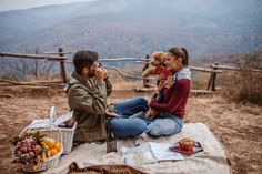 a man and woman sitting on top of a blanket with a teddy bear in their lap