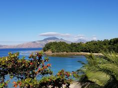 an island with trees and water in the foreground, surrounded by blue sky and clouds