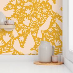 a yellow wall with white flowers and birds painted on it, next to two mugs