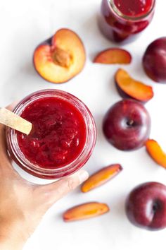 a hand holding a jar of fruit juice next to sliced peaches