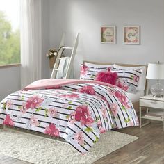 a bed with pink and white flowers on the comforter, next to a window