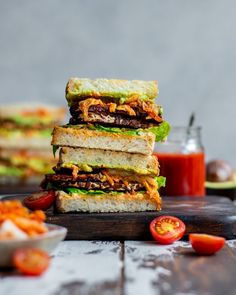 three sandwiches stacked on top of each other with tomatoes and ketchup in the background