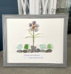 a white frame with some rocks and flowers in the middle, on top of a table