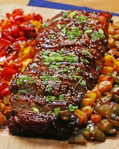 a wooden cutting board topped with meat covered in sauce and veggies on top of it