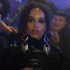 a woman in black leather outfit with large hoop earrings on her head and other people behind her