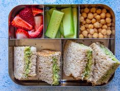 an open lunch box filled with sandwiches, fruit and nuts on the side to eat