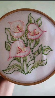 a hand holding a white embroidered object with pink flowers on it and green leaves in the middle