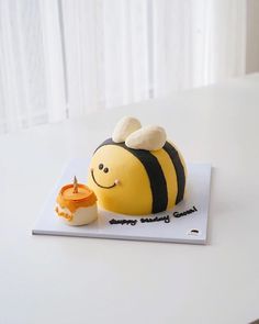 a cake shaped like a bee sitting on top of a white table next to a cup