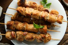 several skewers of meat are on a white plate with garnishes