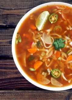 a bowl of soup with carrots, celery and noodles on a wooden table