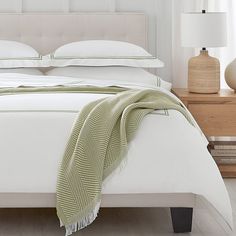 a white bed with green and white blankets on it's headboard in a bedroom