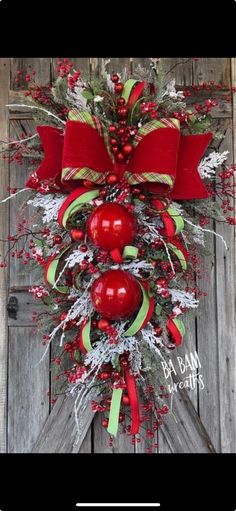 a christmas wreath with red apples and green ribbon hanging on a wooden door in front of an old barn