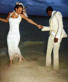 a bride and groom holding hands on the beach at night with clouds in the background