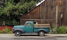 an old blue truck parked in front of a barn