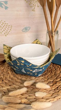 a white bowl sitting on top of a wicker place mat next to wooden utensils