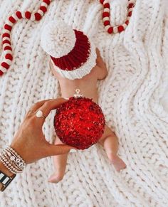 a person holding a red ornament on top of a white knitted blanket