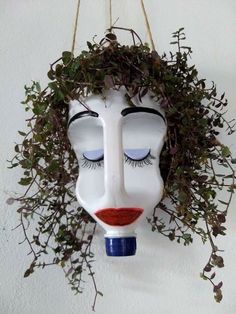 a white mask with blue eyes and red lips hanging on a wall next to a plant