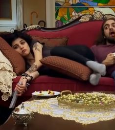 a man and woman laying on a red couch