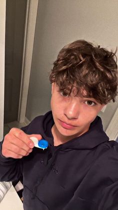 a young boy brushing his teeth with a toothbrush in front of him and looking at the camera