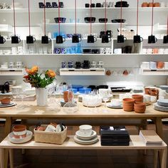 a table with plates, cups and vases on it in a room filled with shelves