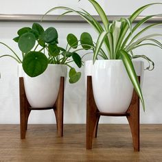 three white planters sitting on top of a wooden table next to each other with green plants in them