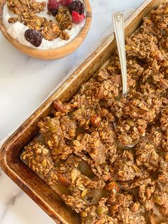 a pan filled with granola next to a bowl of yogurt and raspberries