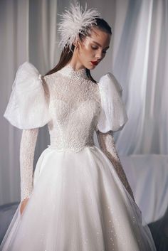 a woman in a white wedding dress with long sleeves and feathers on her head is posing for the camera