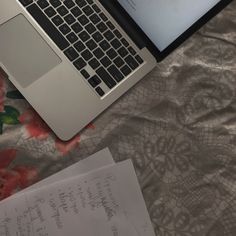 an open laptop computer sitting on top of a bed next to a paper and pen