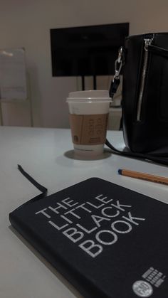 the little black book is next to a cup of coffee and a purse on a table