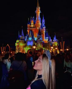 a woman standing in front of a castle at night with lights on it's side