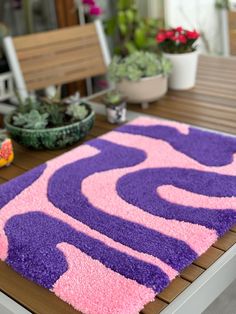 a purple and pink rug sitting on top of a wooden table next to potted plants