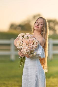 a beautiful young woman holding a bouquet of flowers in her hands while standing on the grass