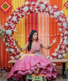 a woman in a pink and yellow dress sitting on a bench with flowers around her