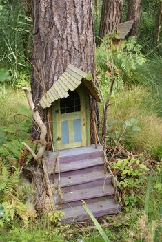 a fairy door in the woods with steps leading up to it and a tree next to it