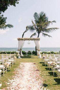 an outdoor wedding setup with white chairs and flowers on the aisle, overlooking the ocean