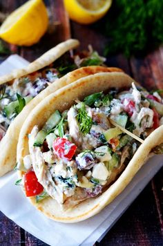 three tacos on a plate with lemon wedges and parsley in the background