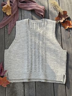 a sweater and scarf laying on top of a wooden floor next to leaves with autumn colors in the background