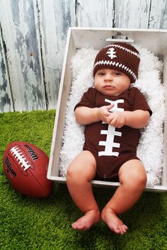 a baby in a football outfit is laying on the grass with a football next to it