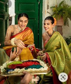 two women in colorful saris are cutting a cake with white flowers on the plate