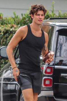 a man in black shirt and shorts walking next to a car with an ice cream cone