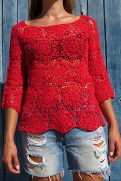 a woman standing in front of a wooden wall wearing ripped shorts and a red top