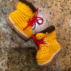 two crocheted yellow shoes with red laces on them sitting on a granite surface