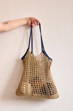 a hand holding a bag hanging on the wall with it's handles up and two hands in front of it