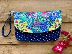 a blue and white flowered purse sitting on top of a wooden table next to red flowers