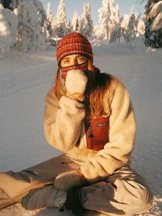 a woman sitting in the snow with her hand on her mouth and wearing a hat