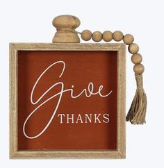 a wooden frame with the words give thanks written in white lettering and a tassel hanging from it