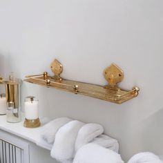 two gold towel racks on the wall above a white mantle with candles and other items